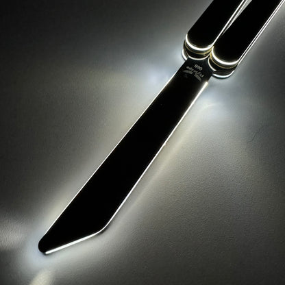 A close-up of a black butterfly knife, also known as a balisong or butterfly trainer, with its blade fully extended. The knife, also referred to as a Sabre, is photographed in low light, with glowing edges reflecting off the polished metal surface. The dark background and soft lighting emphasize the knife’s modern and sleek design.