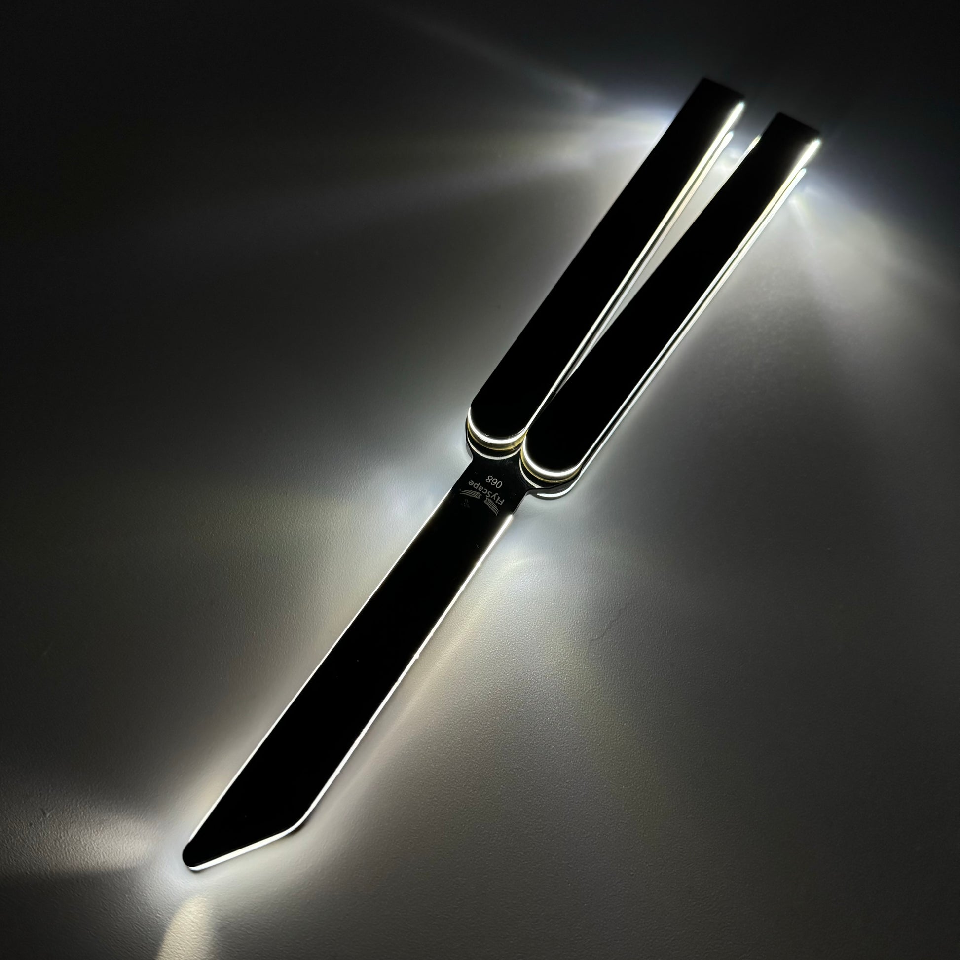 A sleek black butterfly knife, also known as a balisong or butterfly trainer, with sharp edges and extended handles, illuminated dramatically with glowing reflections under low light. The knife, also referred to as a Sabre, is positioned against a dark background, showcasing its modern design and polished metal features.