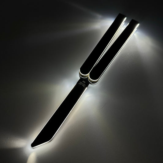 A sleek black butterfly knife, also known as a balisong or butterfly trainer, with sharp edges and extended handles, illuminated dramatically with glowing reflections under low light. The knife, also referred to as a Sabre, is positioned against a dark background, showcasing its modern design and polished metal features.